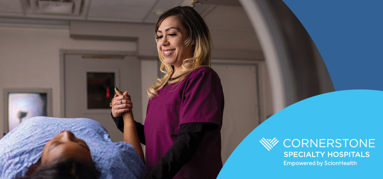 nurse in scrubs holding the hand of a prone patient entering an MRI machine. Cornerstone Specialty Hospitals logo bottom right